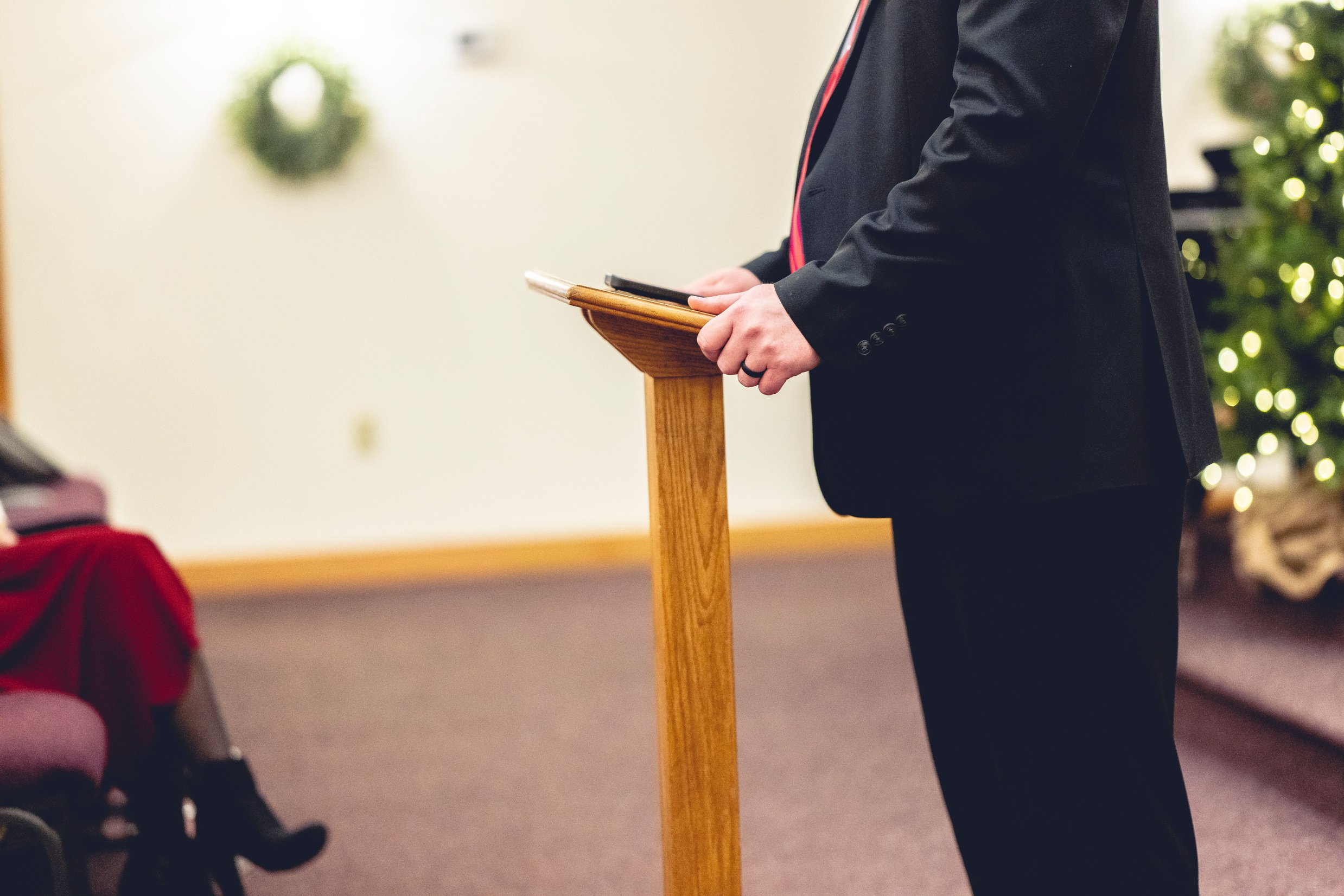 Male wearing a black suit and preaching holding onto a pulpit